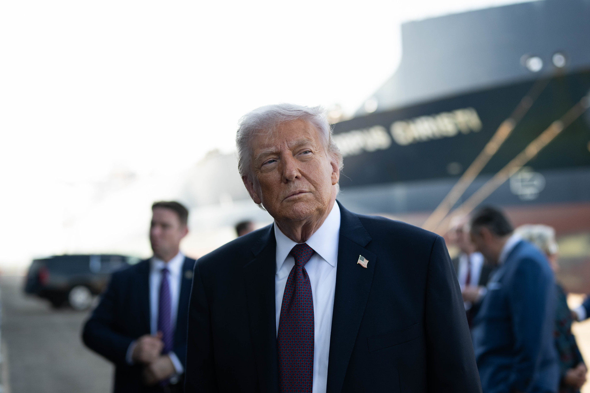 Donald Trump preparing to deliver a speech, with a large shipping vessel in the background.