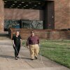 Two people who are blind --- a white, blonde woman with shoulder-length hair and a white man short, dark hair and sunglasses --- are walking on the campus of West Virginia State University while holding canes.