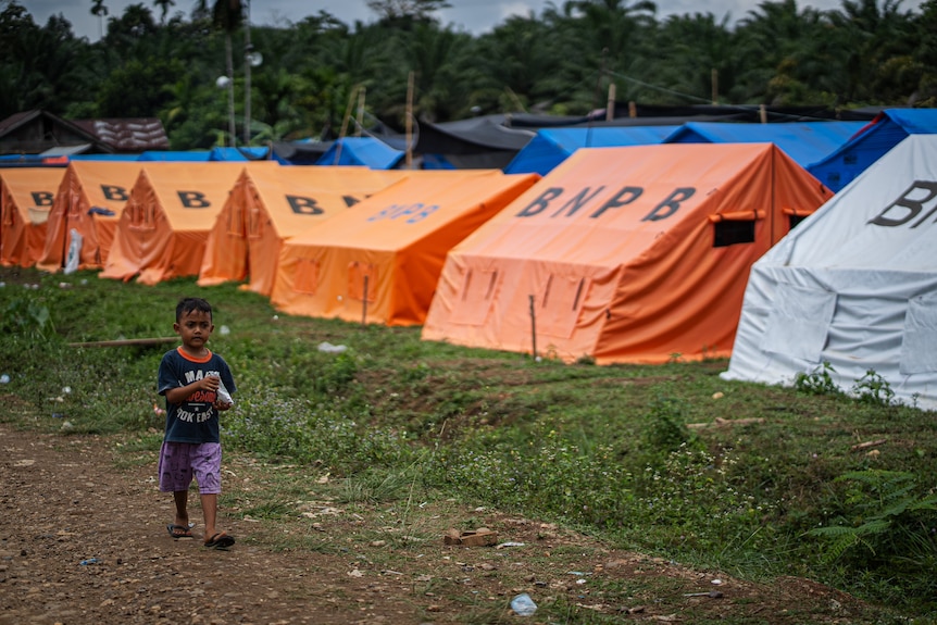 A boy walks past tents housing survivors in Sawang district after the disaster left them homeless.