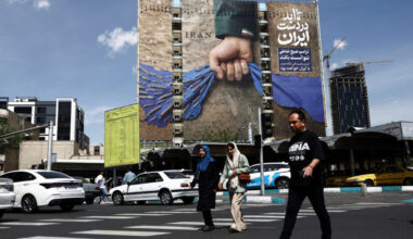 People walk past a billboard with a graphic design about the Strait of Hormuz on a building, in Tehran