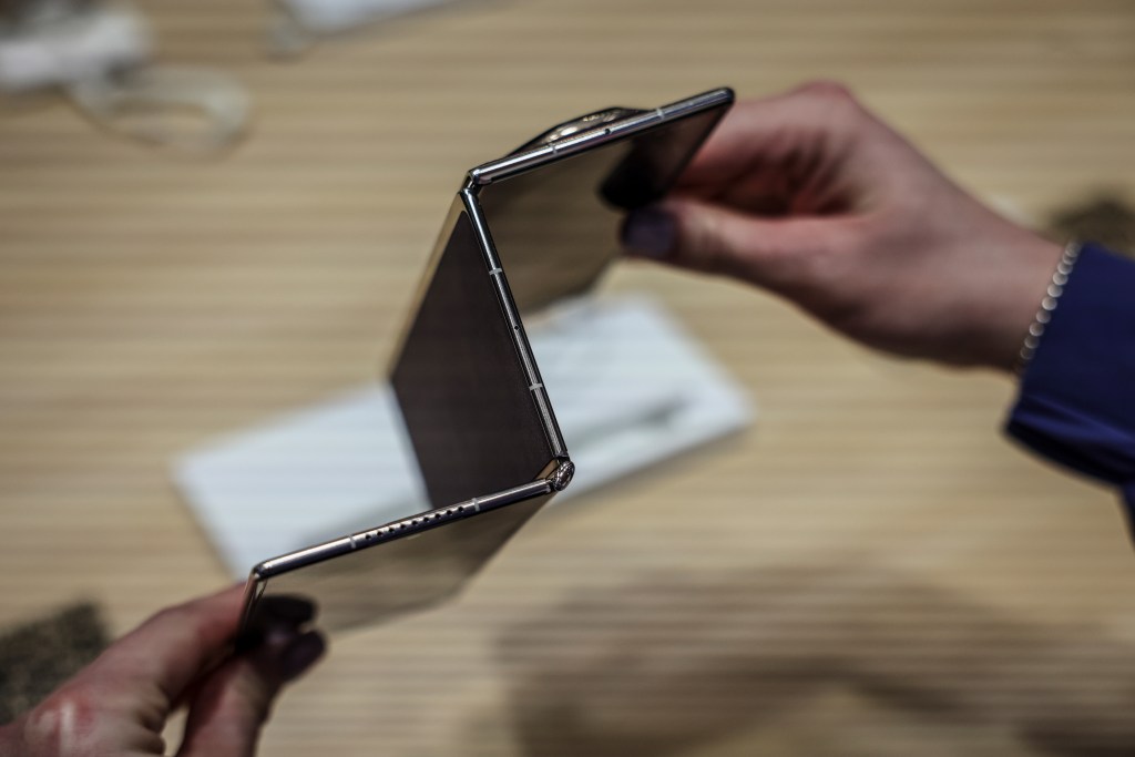 A person holding a Huawei Mate XT tri-fold smartphone, folded twice.