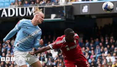 Erling Haaland, wearing Manchester City's light blue kit, celebrates his latest hat-trick by making a three-finger salute with his left hand