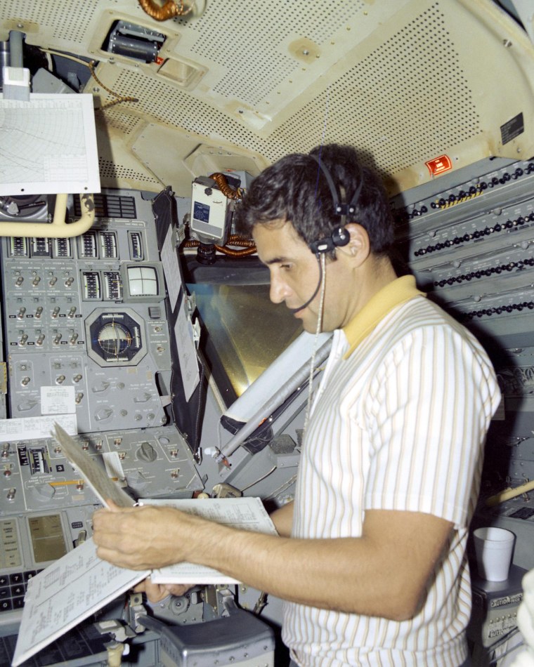 Harrison Schmitt holds documents while standing inside of a lunar module simulator