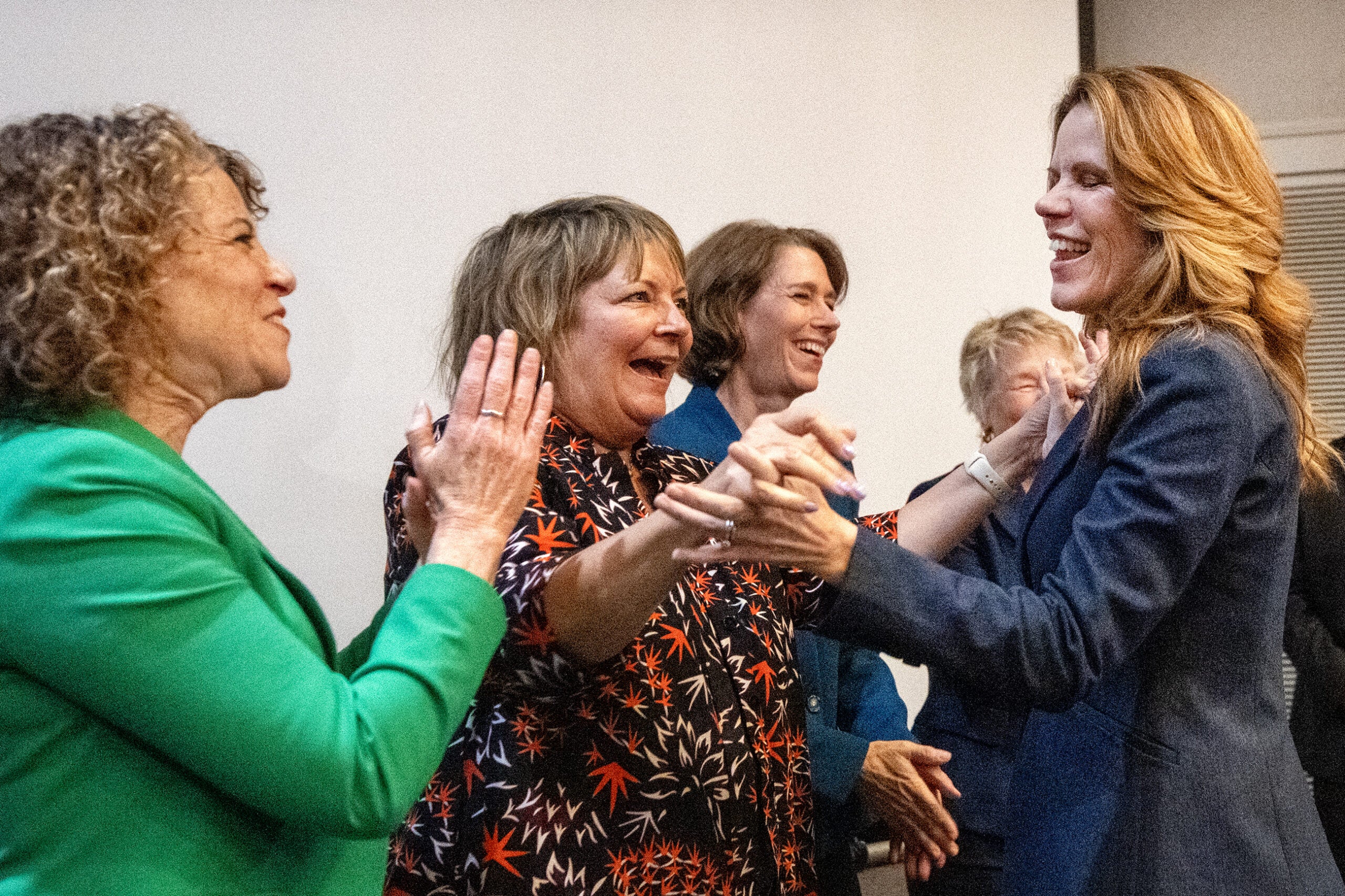 Four women stand together indoors, smiling and holding hands, appearing to celebrate or congratulate each other.
