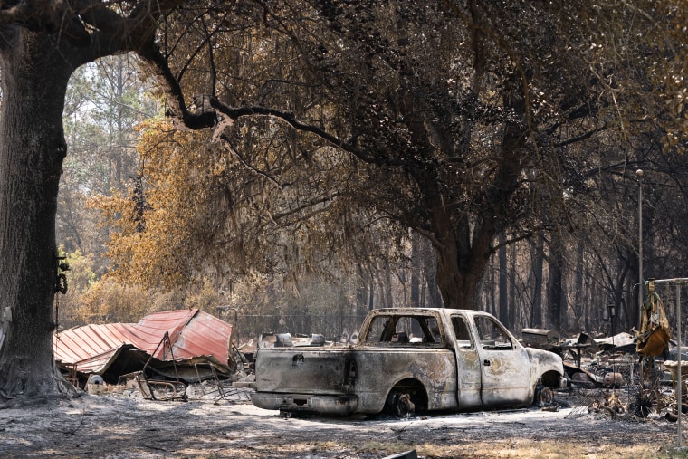 A burned landscape with ash on the ground and a destroyed truck in the foreground.