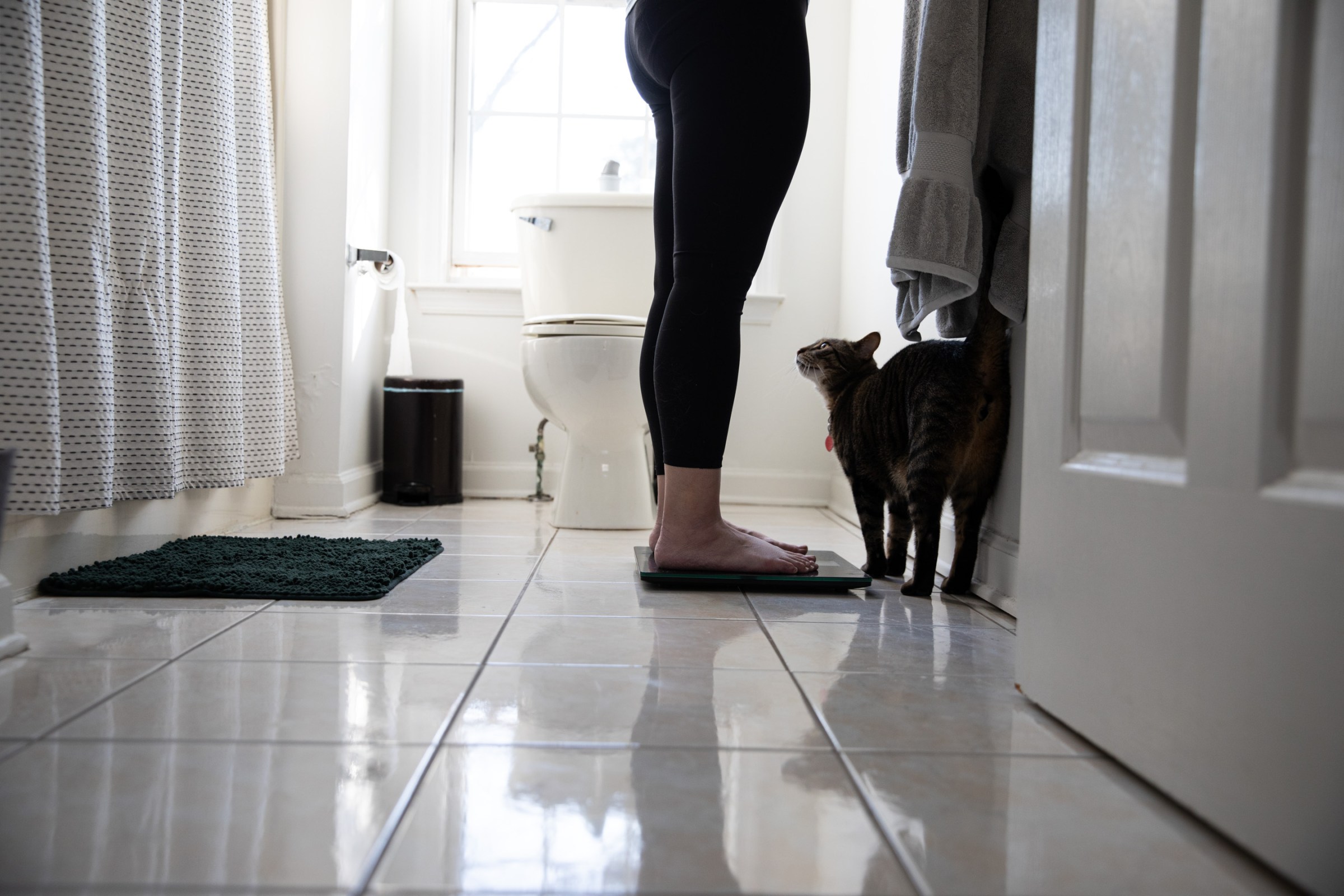 Senior reviewer Victoria Song standing on a scale in a bathroom while a cat looks on