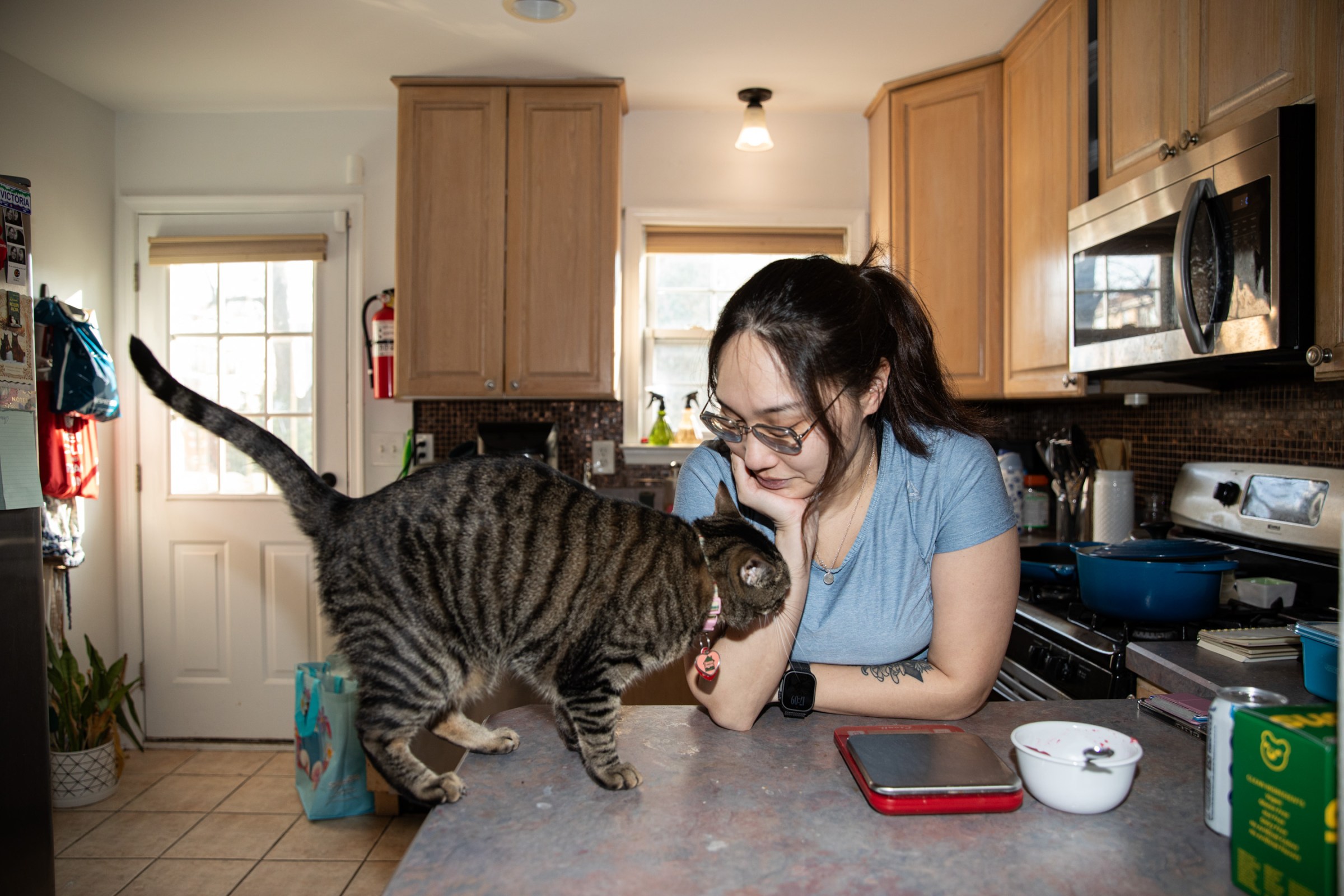 Senior Reviewer Victoria Song looking at a tabby cat on a kitchen counter next to a food scale and bowl.