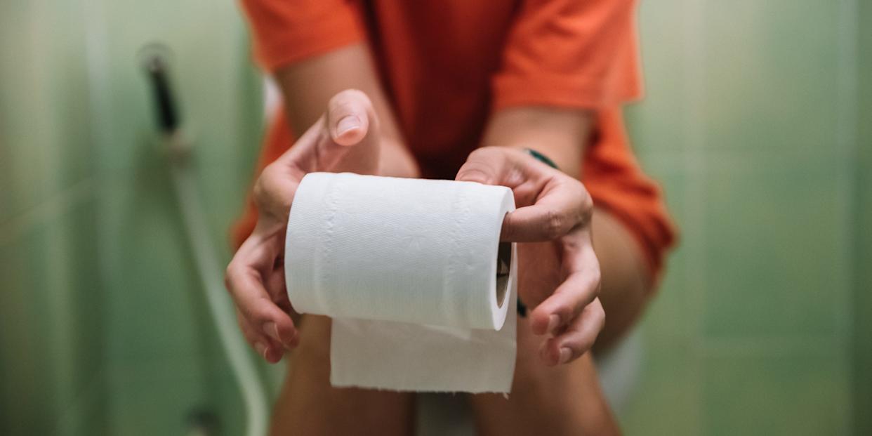 Woman sitting on toilet holding toilet paper roll