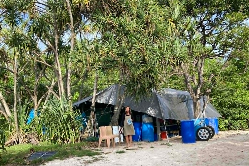 A woman standing in front of a tent and camping area under lots of trees