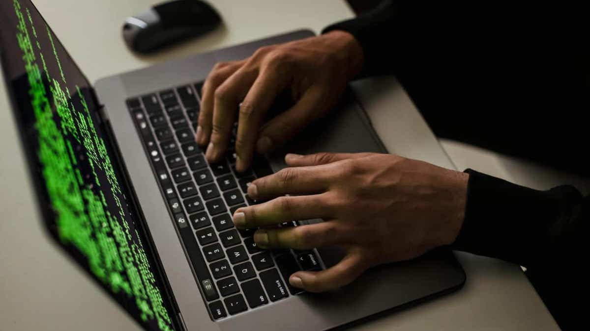 Hands typing on a laptop with green code on the screen