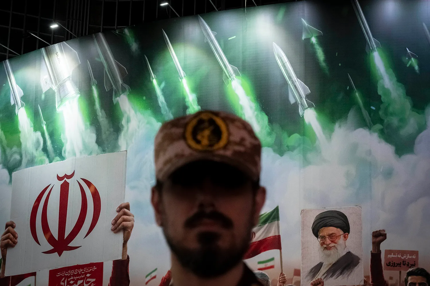 A member of the Islamic Revolutionary Guard Corps stands guard in front of a giant banner depicting images of Iran’s late supreme leader, Ayatollah Ali Khamenei, and ballistic missiles during a pro-government rally in Tehran.