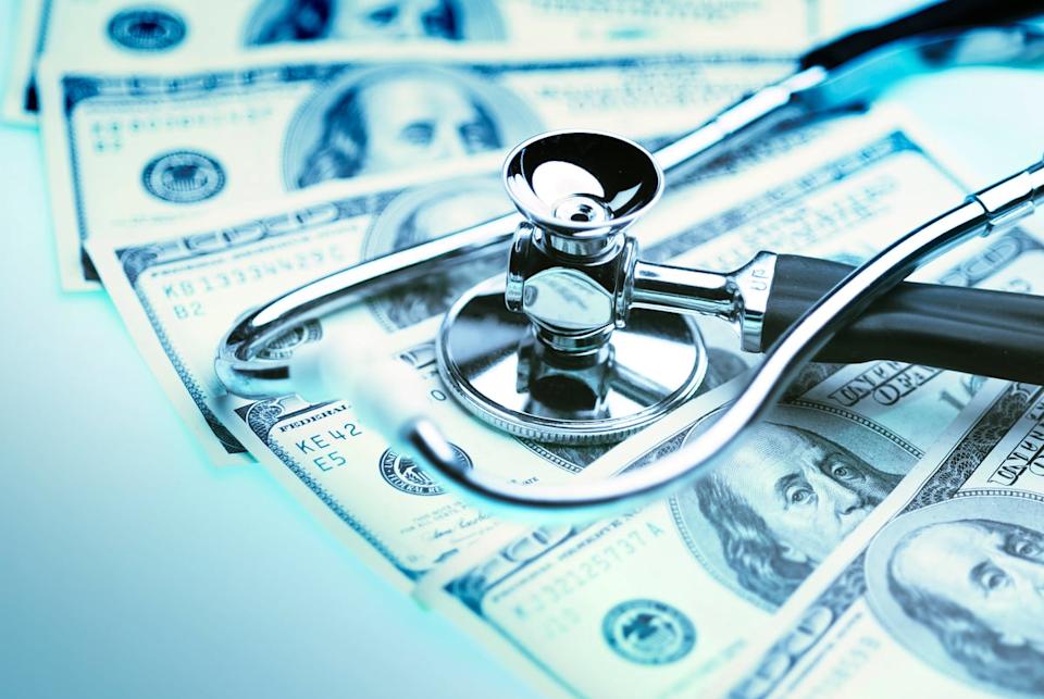 A stethoscope sits atop $100 bills spread across a white table.