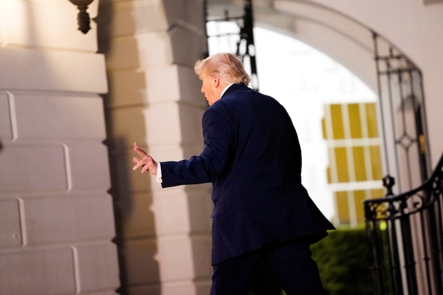 A man in a suit waving and walking. Seen from behind.