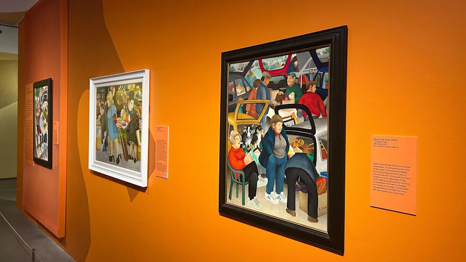 Three pieces of artwork by Plymouth artist Beryl Cook displayed on a bright orange wall. They are all individually framed with little orange signs explaining each painting. 