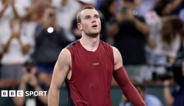 Jack Draper, wearing a maroon vest with a maroon sleeve on his left arm, looks upwards with his mouth open