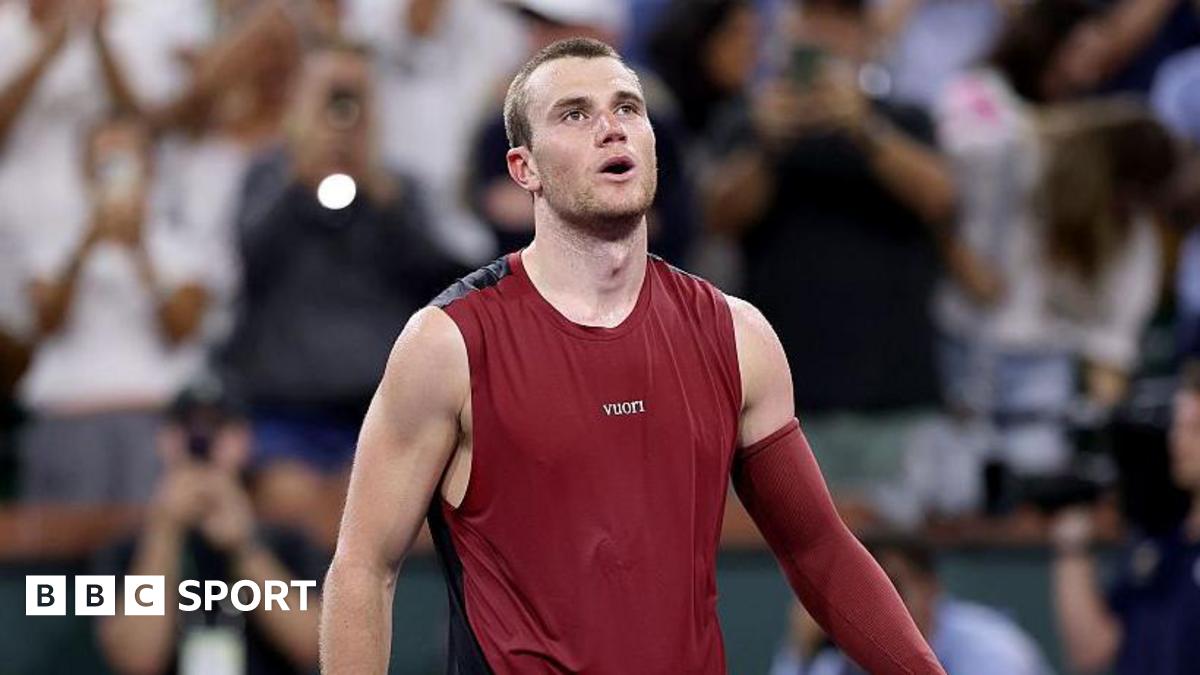Jack Draper, wearing a maroon vest with a maroon sleeve on his left arm, looks upwards with his mouth open