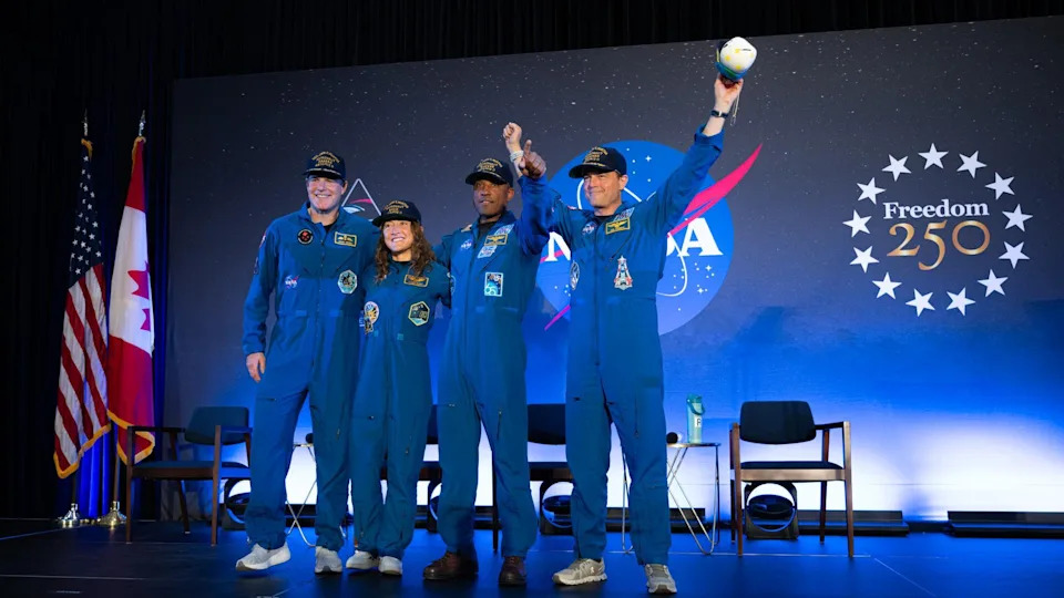 a man in an orange flight suit smiles while carrying a small stuffed moon
