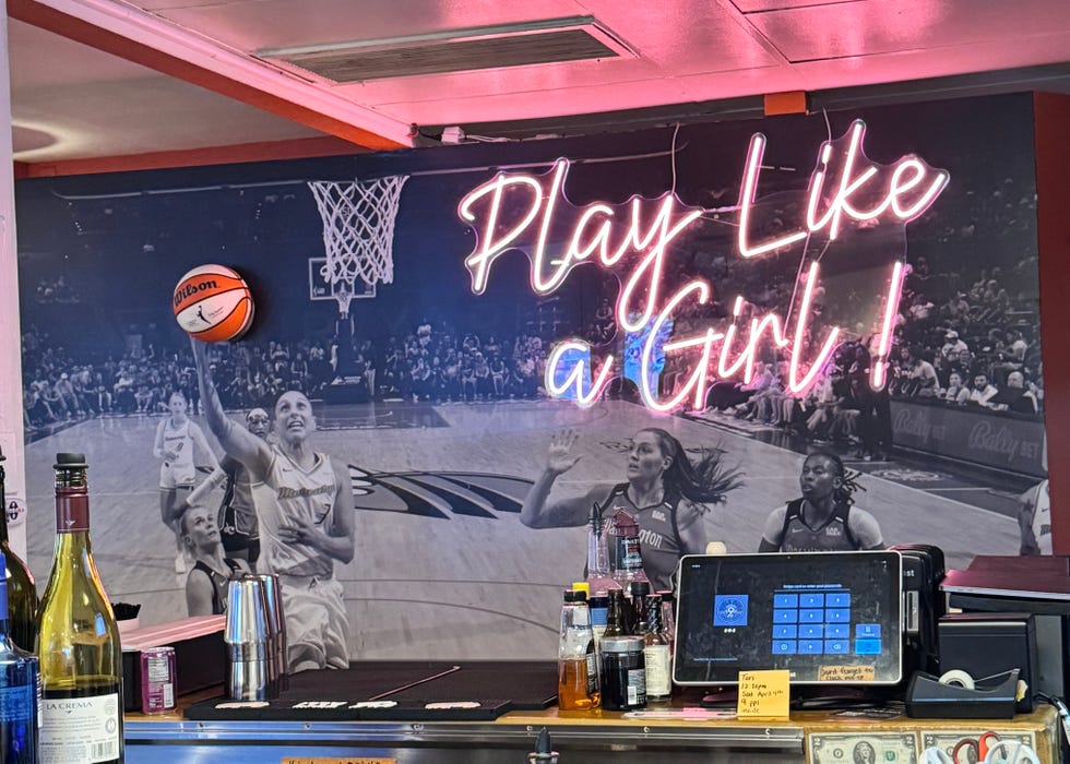 A neon sign with a basketball-themed mural in the background.