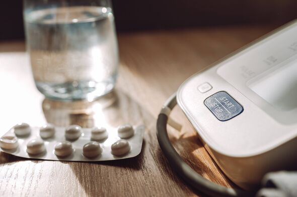 Home blood pressure monitor with pills and glass of water on wooden table for medical care