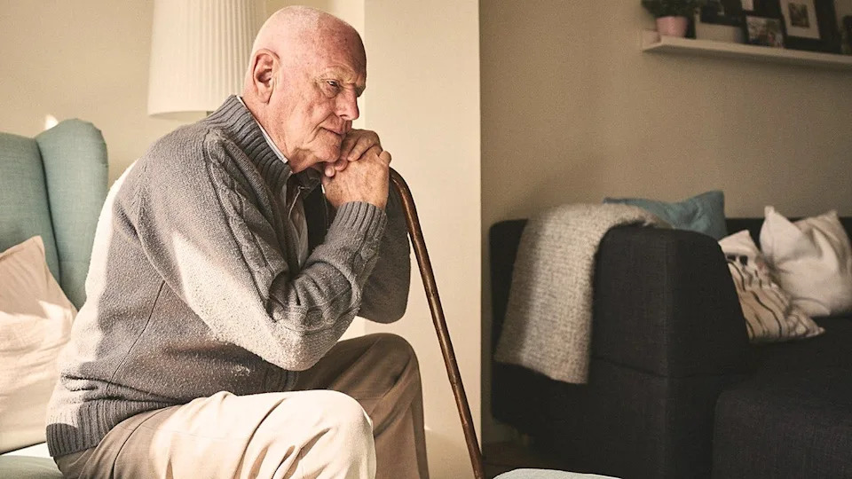 Thoughtful elderly man sitting alone at home with walking cane
