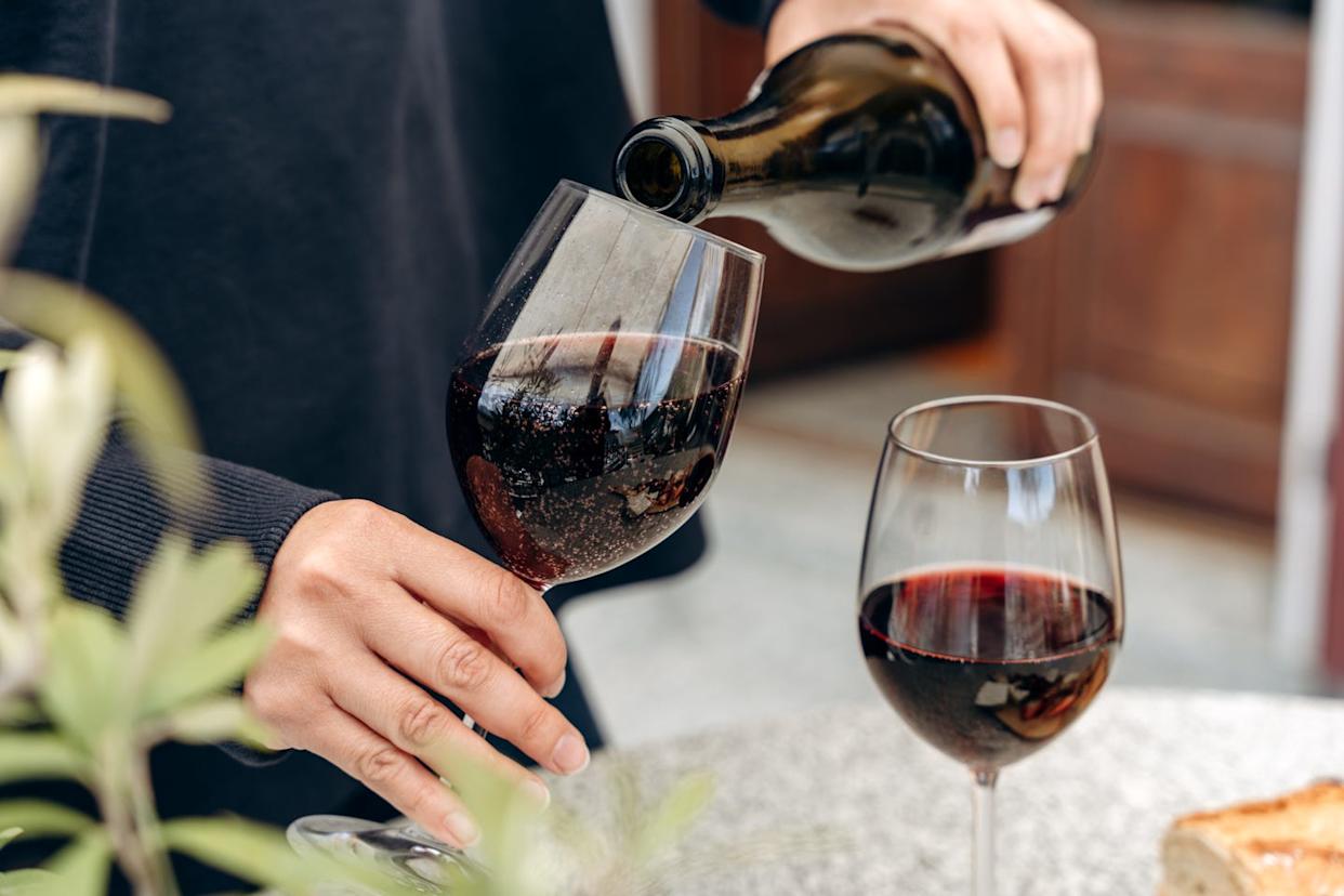 female hands pour red sparkling wine from a bottle into a glass, for an aperitif on the terrace