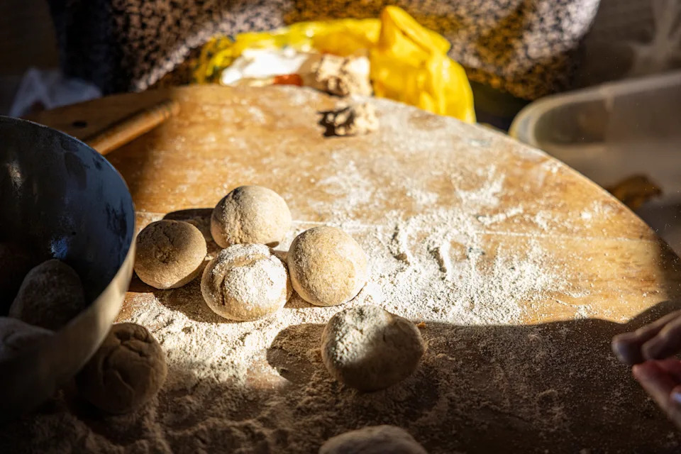 Dough balls on a floured wooden surface suggestive of baking in progress. A mixing bowl and ingredients are partially visible in the background