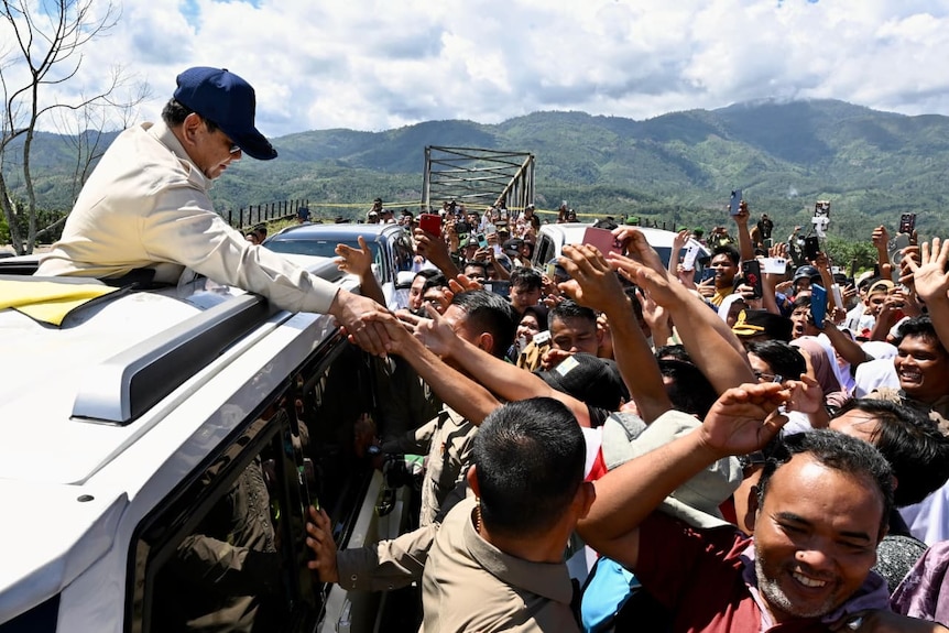 Prabowo reaching out from his vehicle to touch the hands of locals.