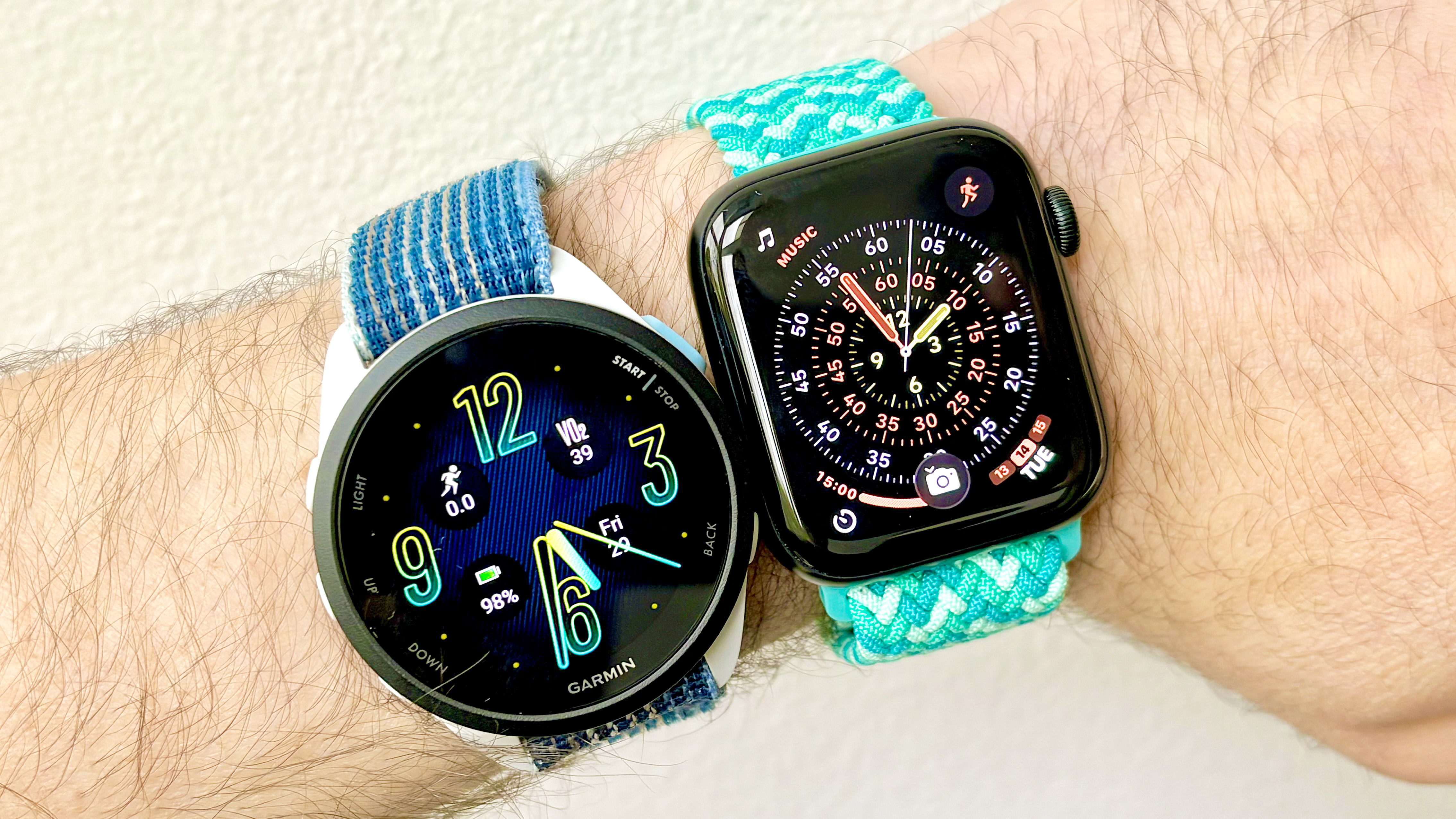 Close-up of the Garmin Forerunner 165 next to the Apple Watch SE 3