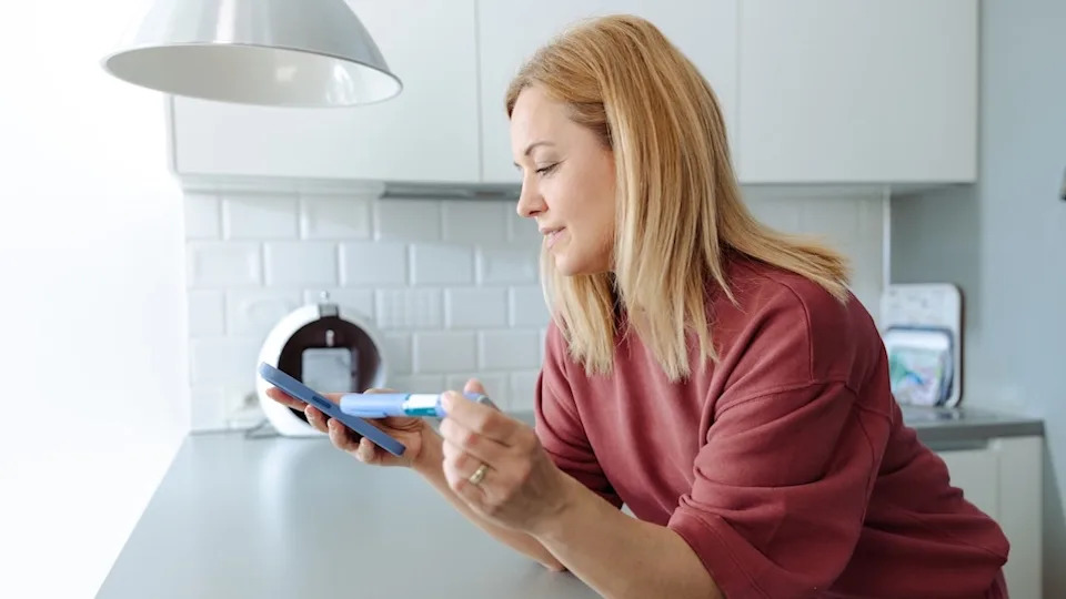 Middle aged woman holding insulin pen and smartphone at home