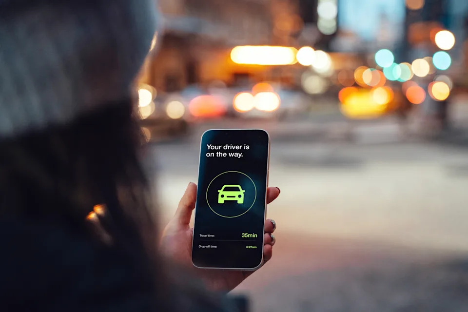 Person holding a smartphone showing a ride-hailing app screen with a notification that the driver is on the way