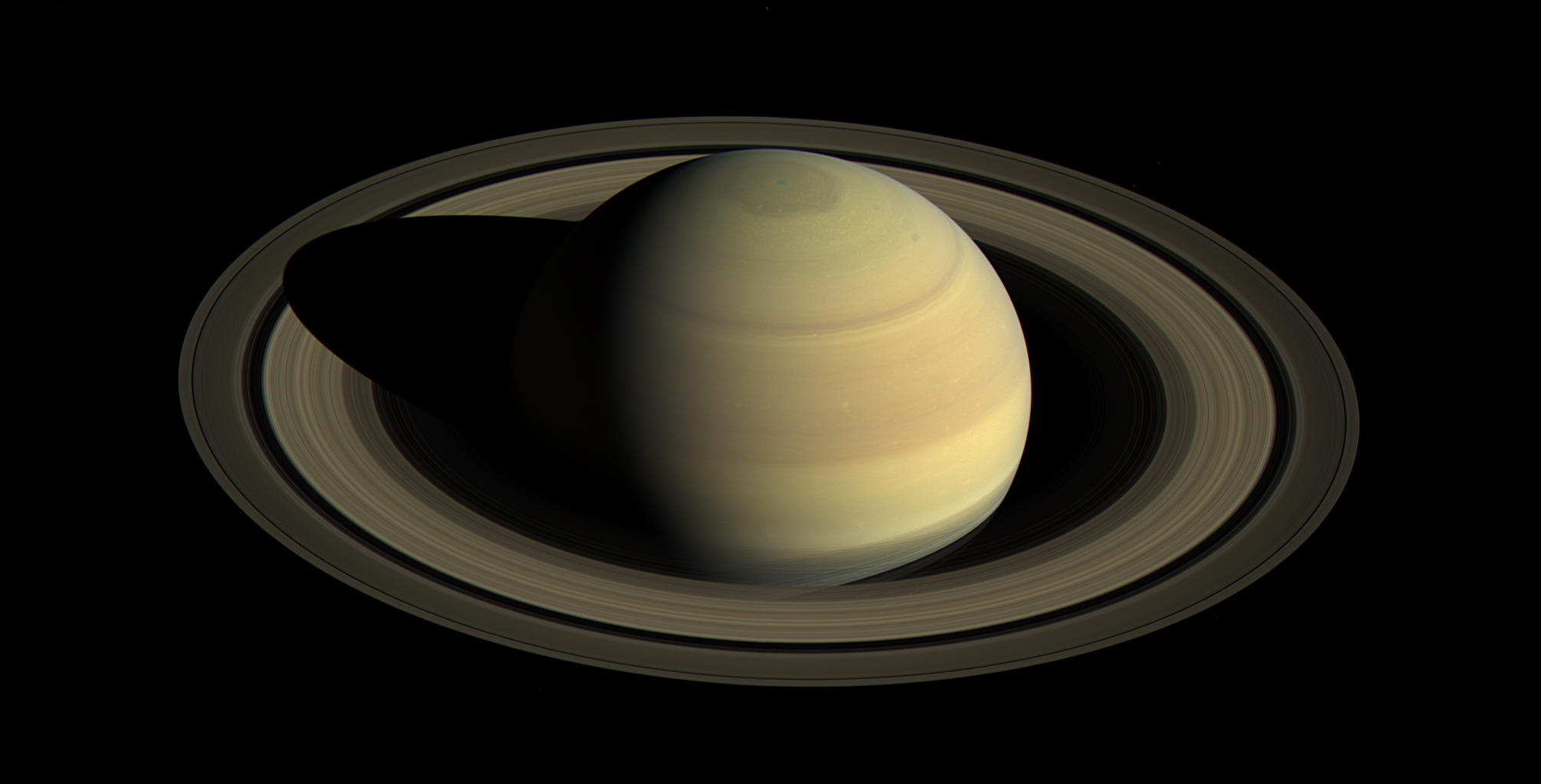 Saturn is shown with its rings, photographed against a black background. The planet's shadow falls across part of the rings.