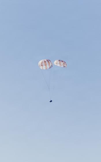 The Orion spacecraft parachutes from the sky.