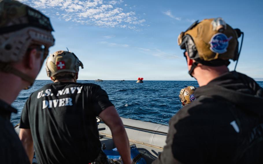 Navy divers approach the Orion capsule in the water.