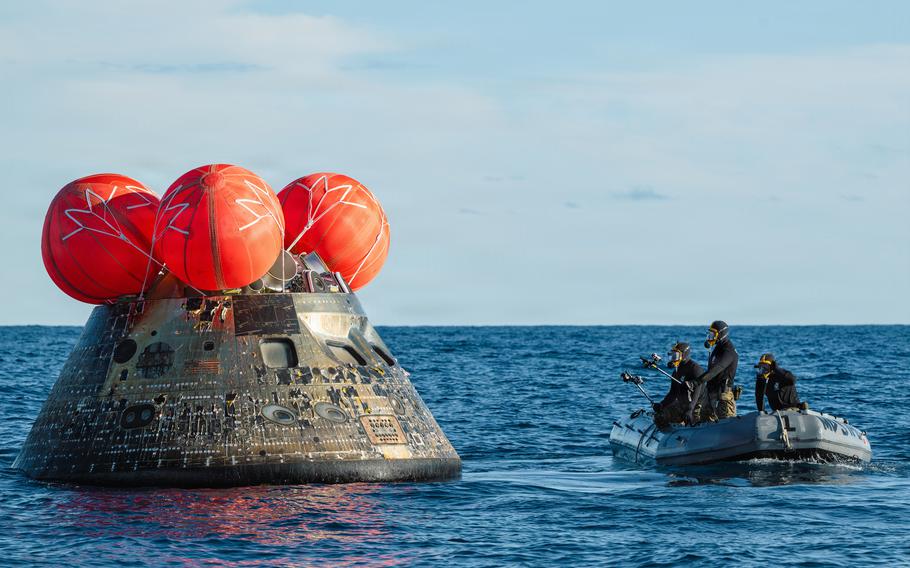 Navy divers approach the Orion capsule in the water.