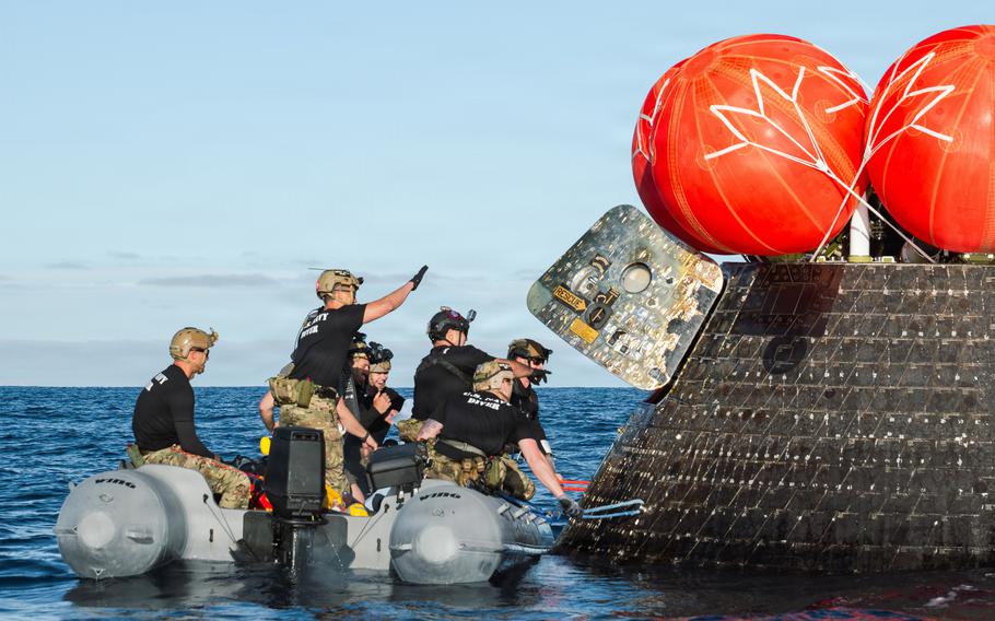 Navy divers open the hatch of the Orion capsule.