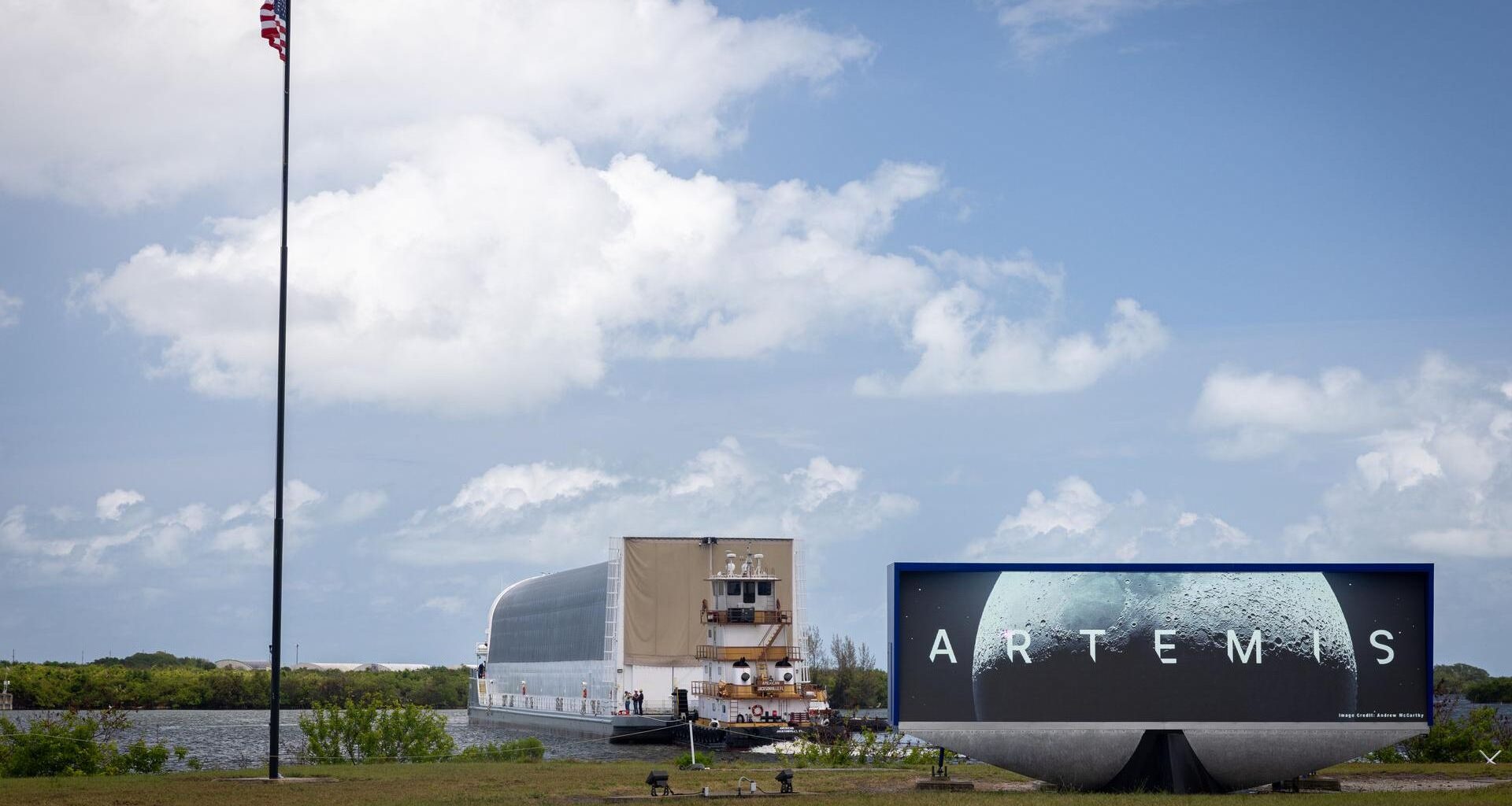 a large barge pulls up to a grassy bank next to a sign that says "artemis"