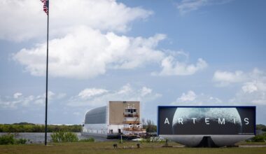 a large barge pulls up to a grassy bank next to a sign that says "artemis"