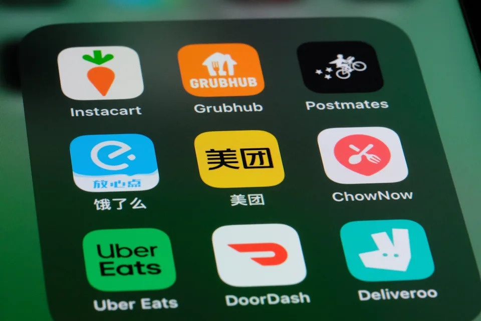 Smartphone screen showing various food delivery app icons, including Instacart, Grubhub, Postmates, Uber Eats, DoorDash, and Deliveroo