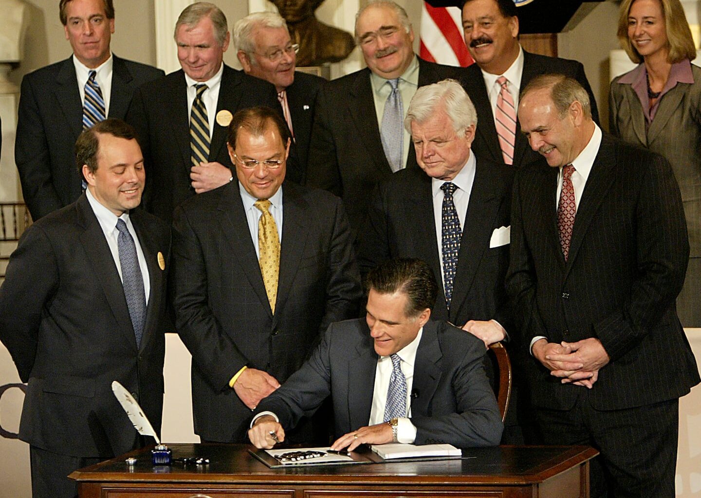 Governor Mitt Romney signed the health care bill as political leaders looked on in 2006.