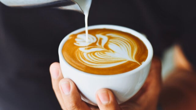A barista's hands pouring a latte into a white cup