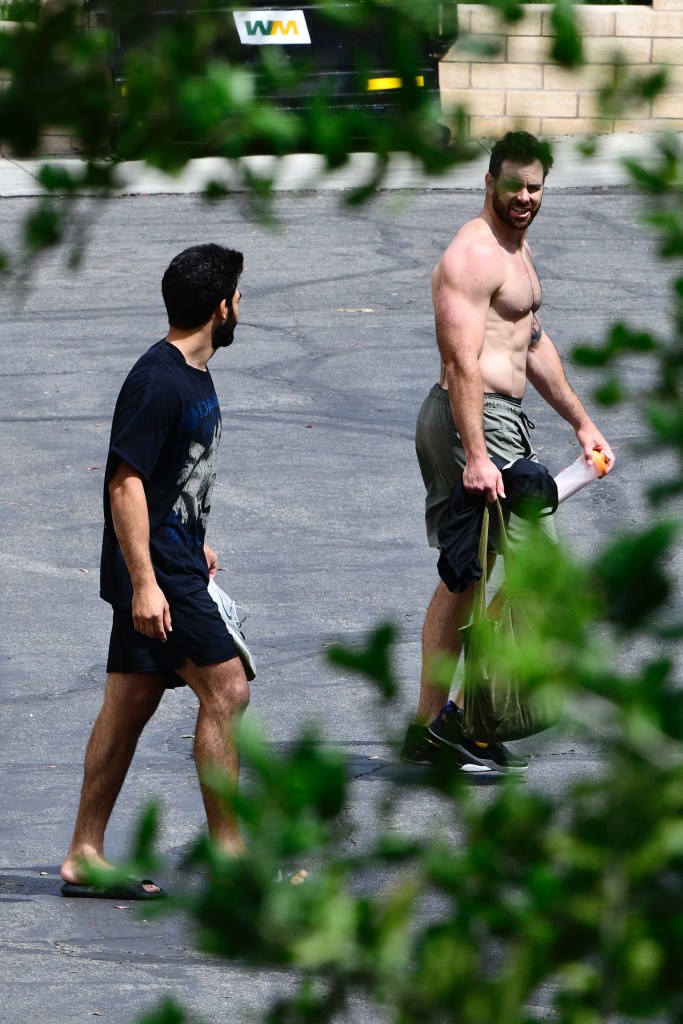 Puka Nacua, shirtless, carrying a water bottle and bag, walks next to a man in a black t-shirt and shorts.