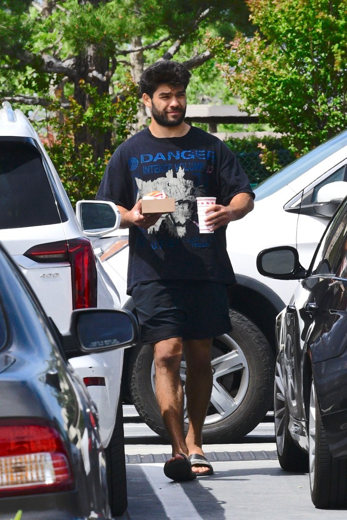 Puka Nacua holding an In-N-Out burger and drink while walking in a parking lot.