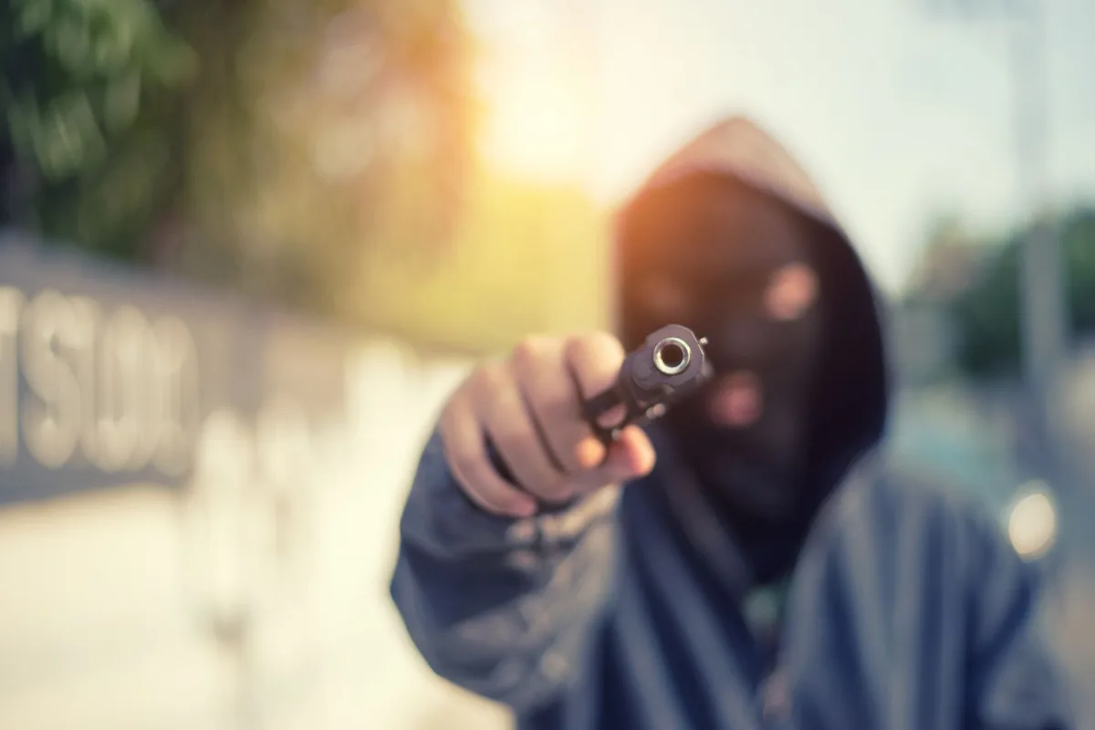 Person wearing a balaclava pointing a gun