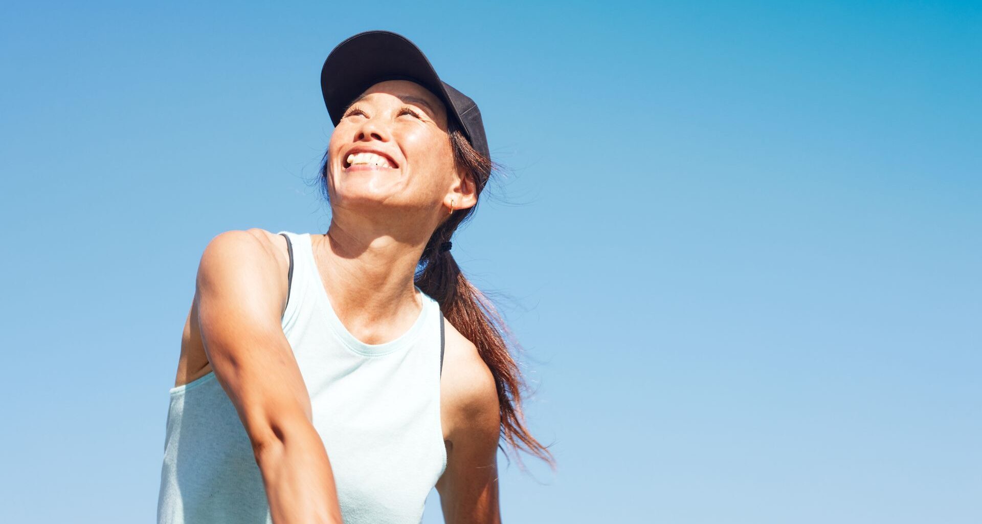 Happy woman wearing sports cap and top playing tennis in the sunshine