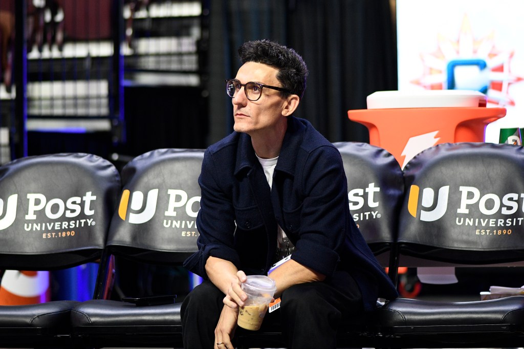 A man in glasses holds a drink while sitting on a bench at the New York Liberty at Connecticut Sun WNBA game.