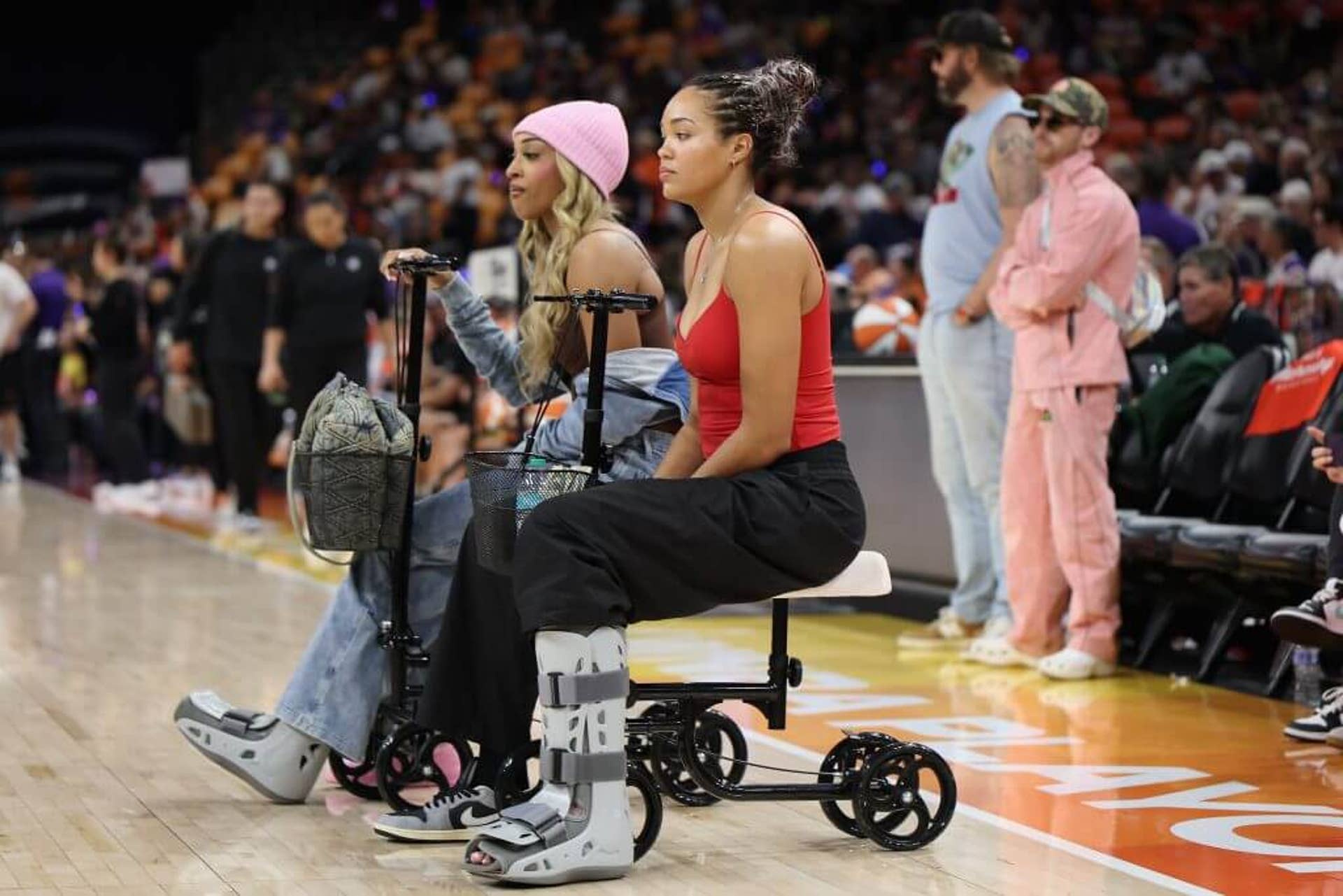 DiJonai Carrington and Napheesa Collier of the Minnesota Lynx watch warmups while sitting on scooters in medical walking boots.