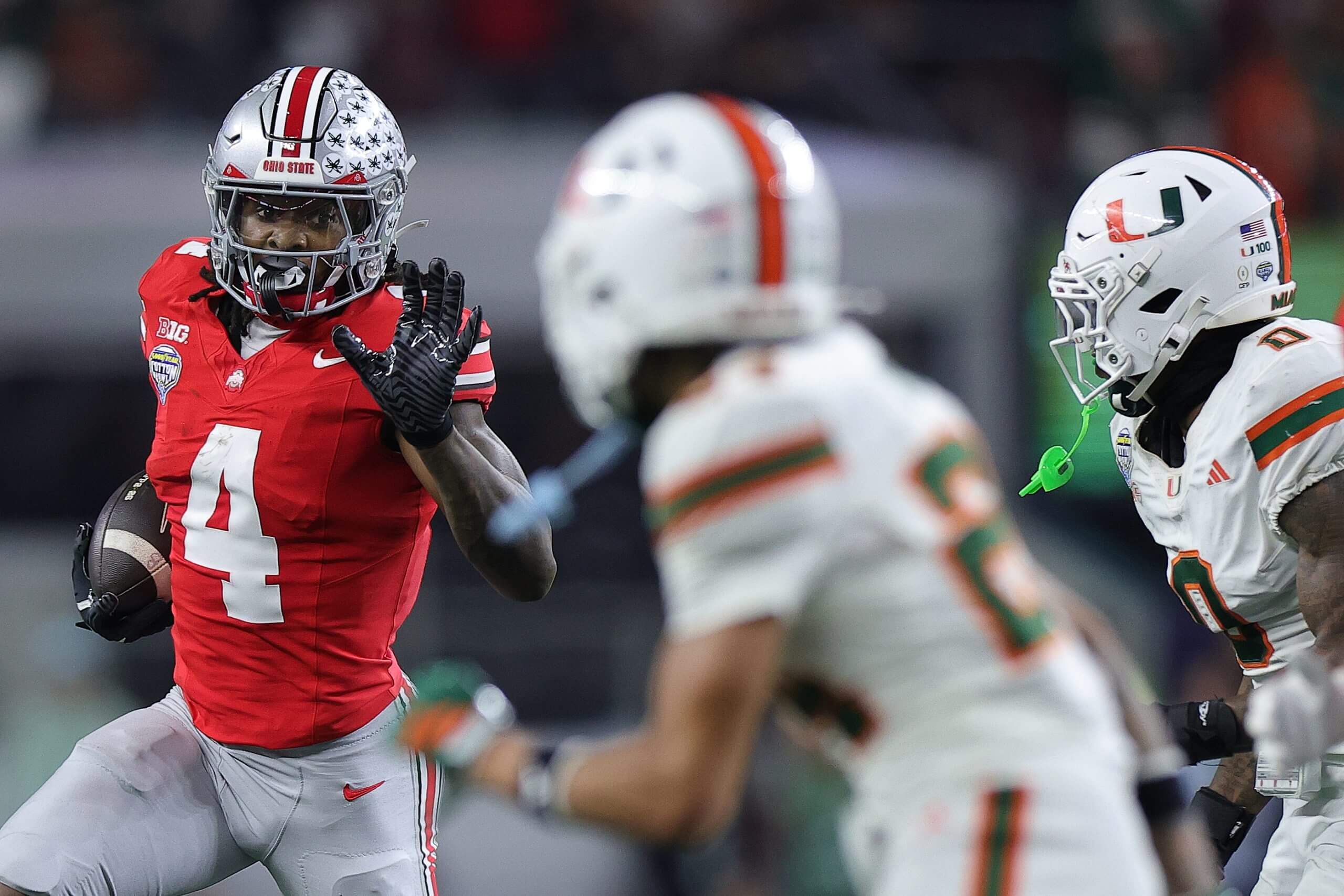 Jeremiah Smith runs with the football and reaches out his left hand against two Miami defenders