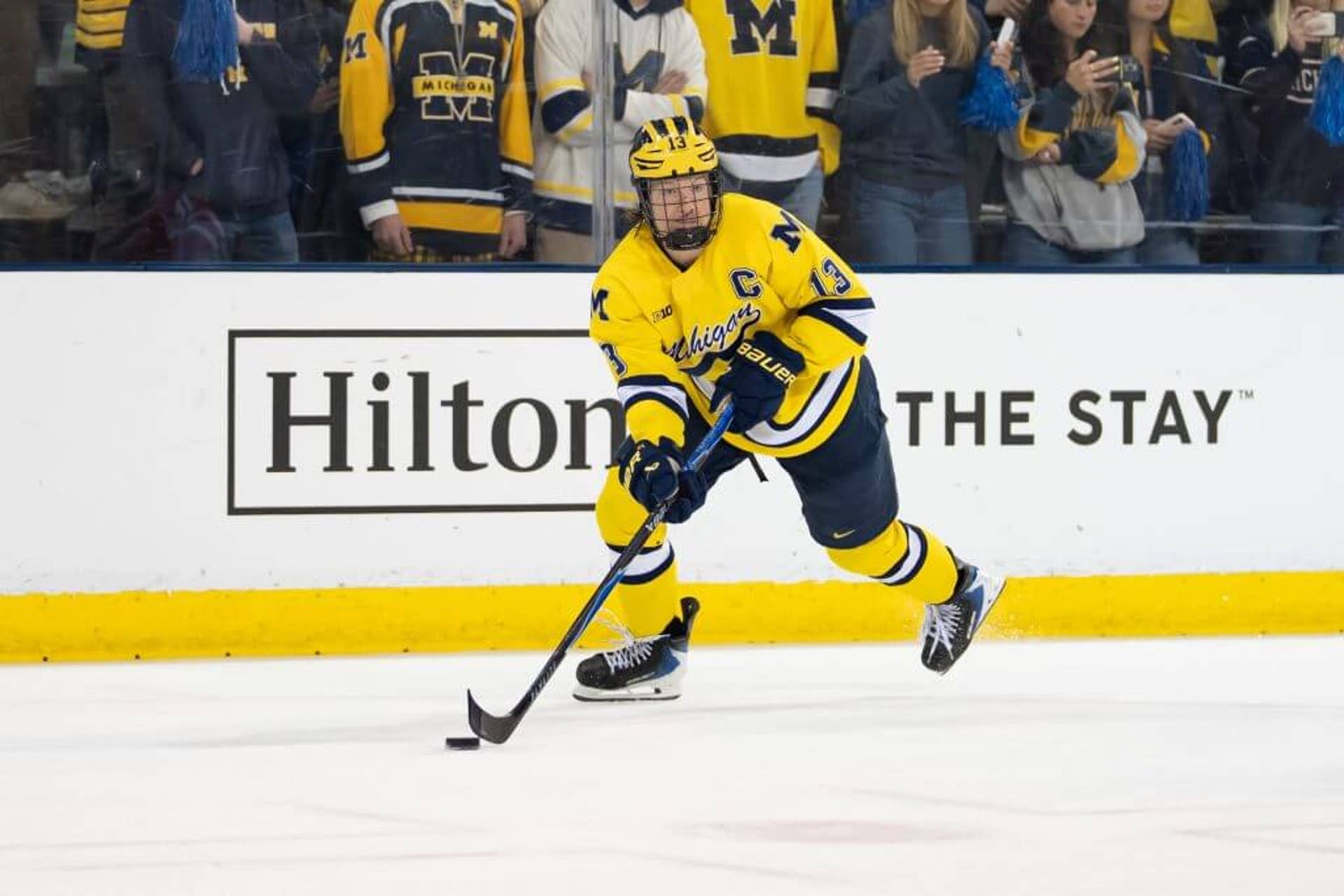 T.J. Hughes #13 of the Michigan Wolverines skates with the puck near the boards.