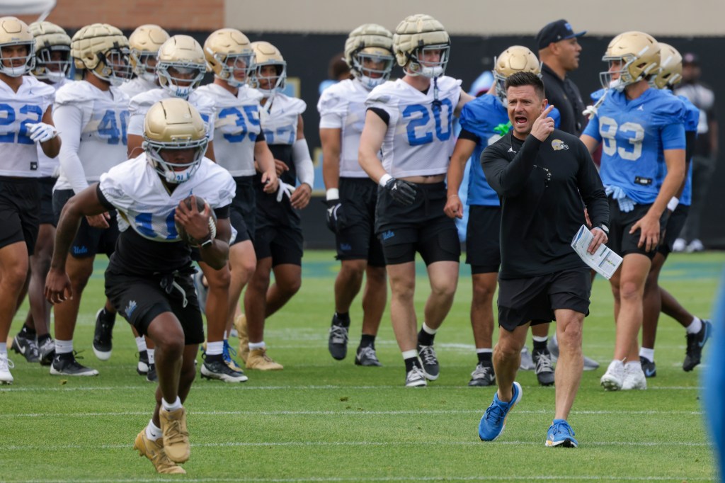 A football player carrying a football, running with other players and a coach on a field.