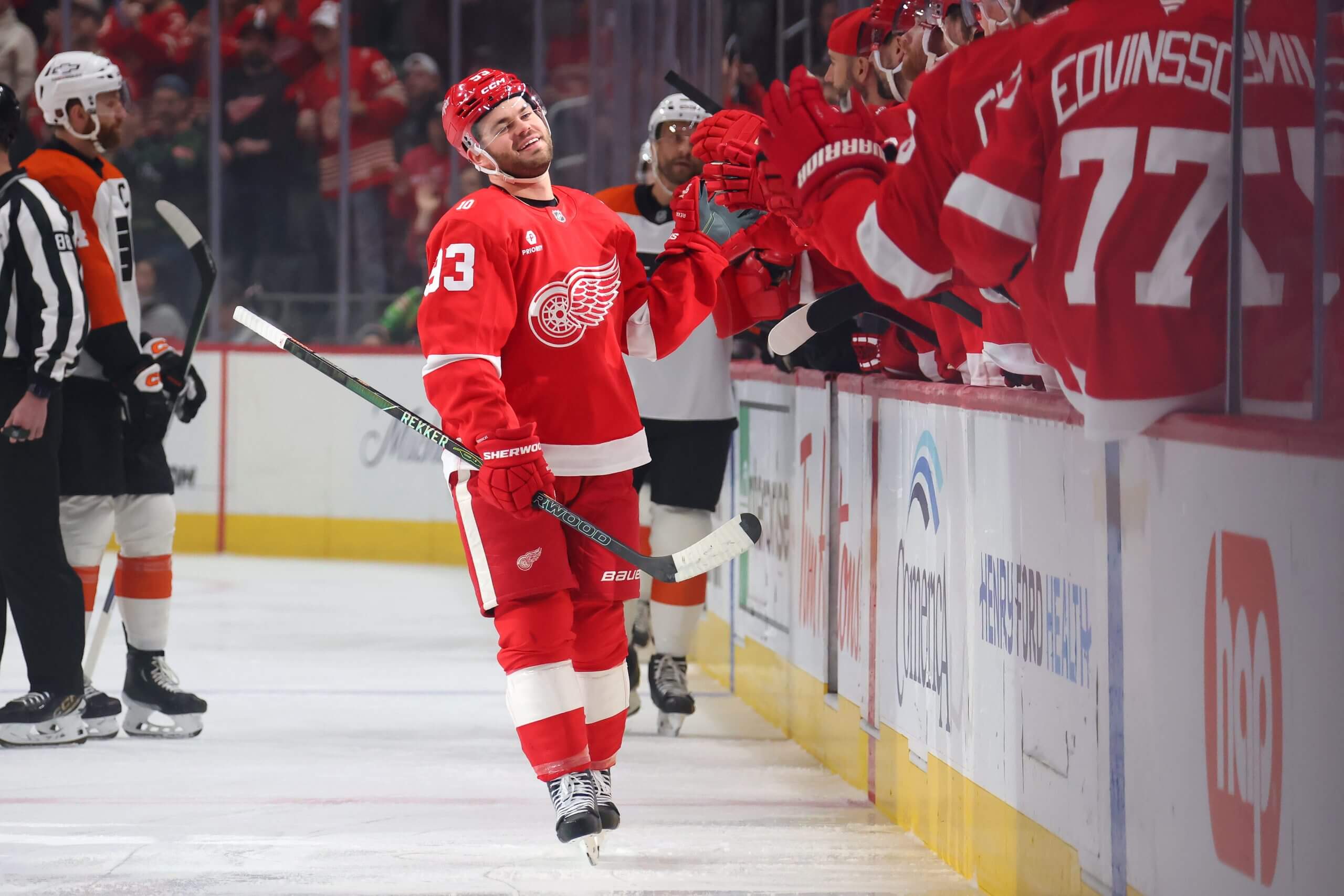 Alex DeBrincat smiles while making his way down the Red Wings fist-bump line.